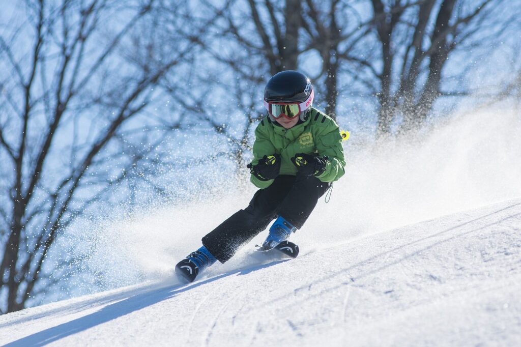 Ein Kind fährt mit seinen Skis bei Sonnenschein eine Piste herunter.